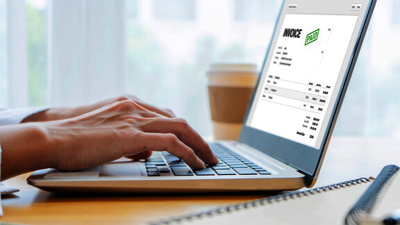 A person typing on a laptop displaying an invoice marked as 'PAID' on the screen