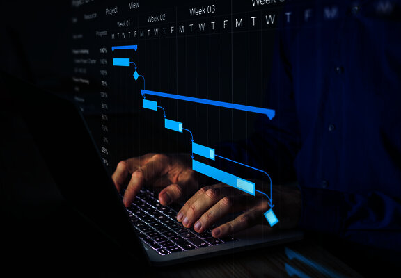 Person working on a laptop with a digital project timeline and task schedule overlay.