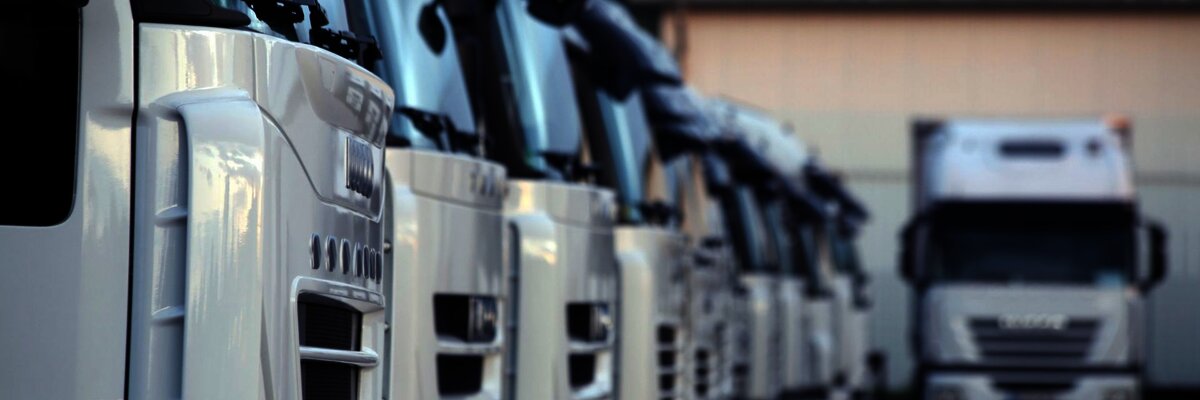 Close-up of a row of white trucks parked in a logistics yard, with one truck in focus in the background, emphasizing fleet management and transportation