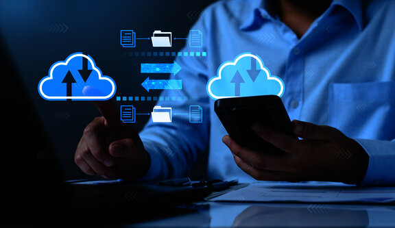 Person using a smartphone and laptop with cloud upload and data synchronization icons.