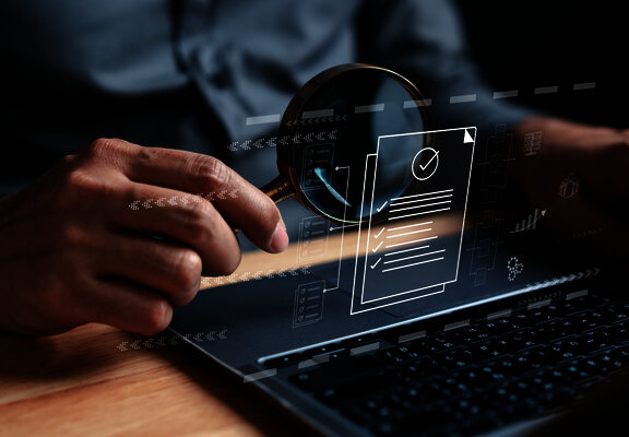 Person using a magnifying glass to review a digital document on a laptop screen.